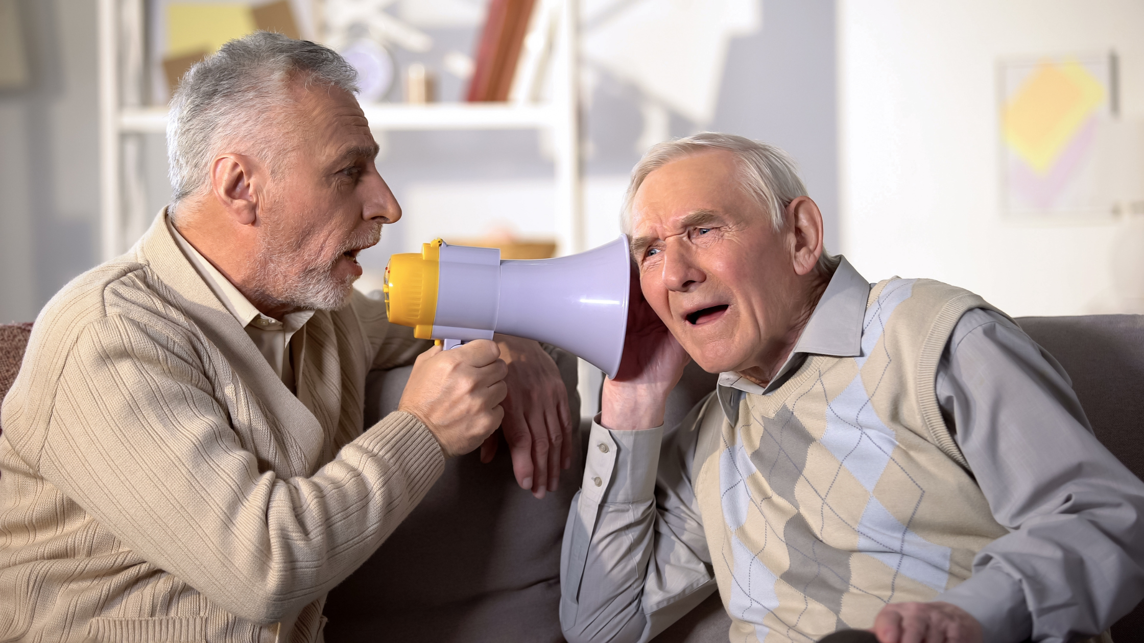 senhor fala com um megafone no ouvido de outro com perda auditiva profunda